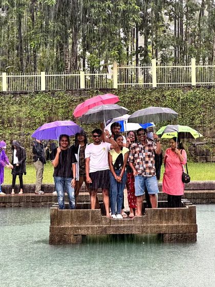 A group enjoying the rain at the Devagange temple pond, holding umbrellas.