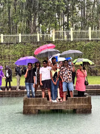 A group enjoying the rain at the Devagange temple pond, holding umbrellas.