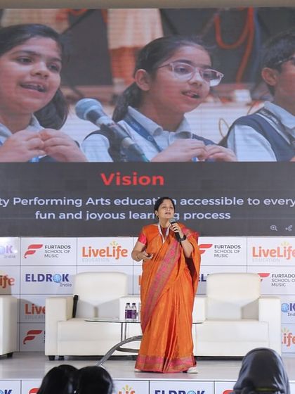 During a presentation to education leaders, I showcase my vision for making quality performing arts education accessible to everyone. The screen behind me highlights our structured curriculum and joyful learning process.