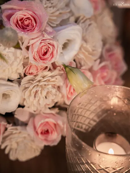 An intimate close-up of soft pink roses and the warm glow of a candle, capturing the romantic and personal essence of an elegant evening affair.