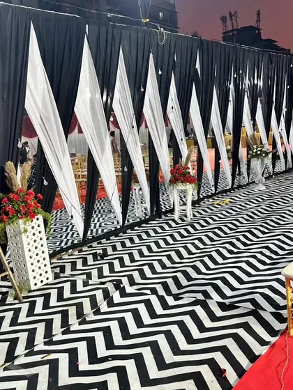 We transformed a large outdoor ground for a corporate gala with this dramatic entrance. The design features a bold black and white chevron pattern floor, contrasting fabric drapes, and ambient string lighting to create an impactful first impression.
