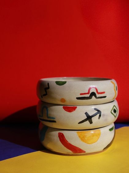 A stack of bowls from the 'Playful Mornings' collection, decorated with colorful zodiac signs and abstract shapes.