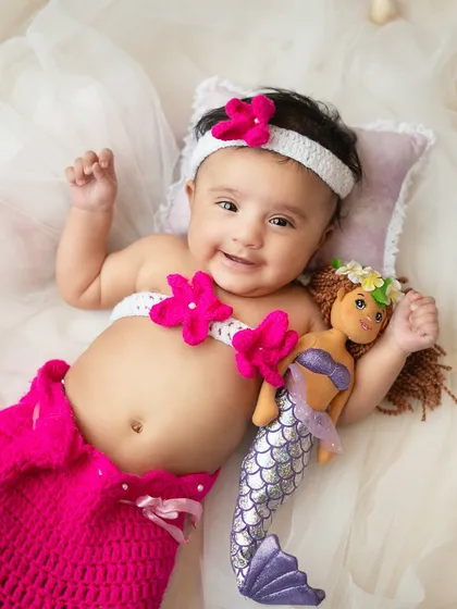This happy little mermaid is all smiles. The setup includes seashells and flowing blue fabric to create an under the sea feel.