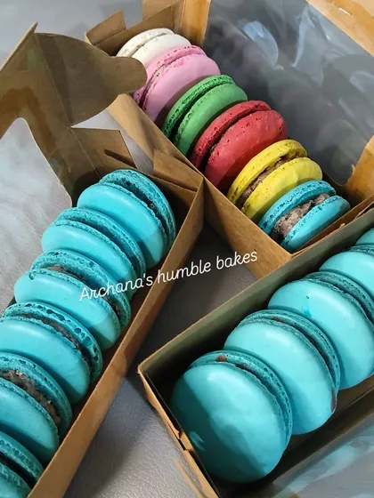 My eggless macarons are a rainbow of flavors, perfect for gifting. Here you can see them packed in custom boxes, with vibrant colors like sky blue, sunshine yellow, and pretty pink, each with a delicious filling.