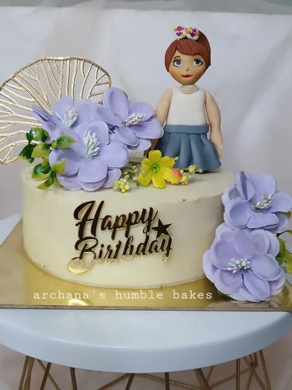 A beautiful cake topped with a hand-molded fondant girl and purple sugar flowers.