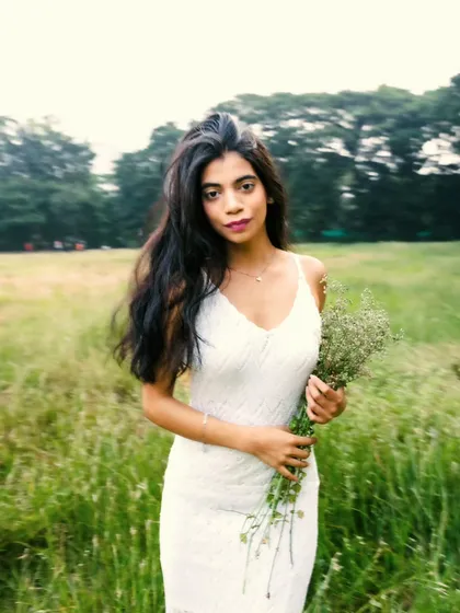 A beautiful, direct-to-camera portrait holding wildflowers. The motion in the background gives a sense of a breezy, open field.