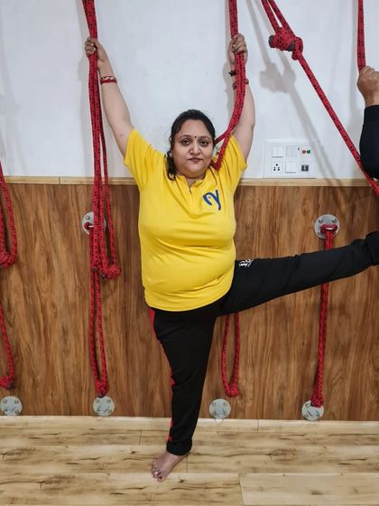 A student uses the wall ropes to practice a standing split variation (Urdhva Prasarita Eka Padasana). The ropes provide support, allowing for a deeper hamstring stretch and improved balance.