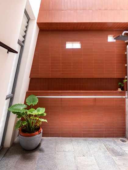 The shower area is defined by a wall of terracotta tiles, adding warmth and texture to the space. The large potted plant thrives in the humid environment, bringing a touch of the outdoors inside.