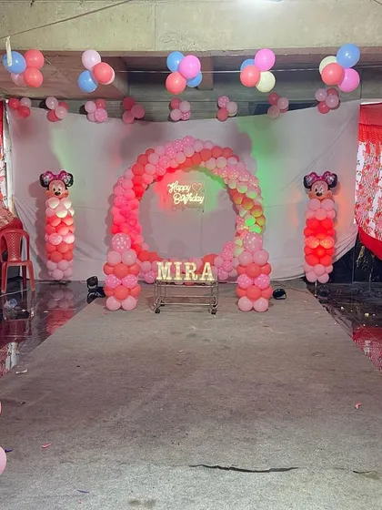 An indoor Minnie Mouse themed birthday setup with a pink balloon arch and character pillars, perfect for a first birthday.