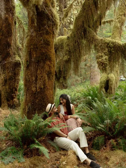 A wide shot of the couple relaxing together in the enchanting rainforest. The moss-covered trees and lush ferns create a magical, fairytale-like atmosphere for their elopement.