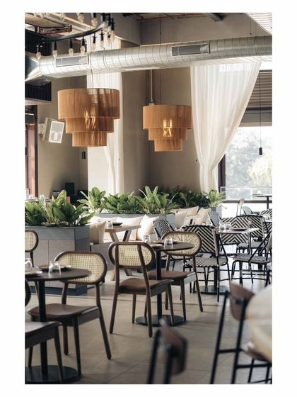 The mix of cane-back chairs and patterned bistro chairs adds visual texture and variety. Sheer white curtains soften the industrial edges and help control the natural light throughout the day.