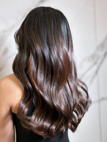 A back view of the hair against a marble wall, highlighting the rich tones and glossy waves.