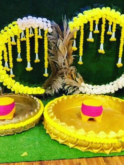A modern and minimalist Haldi setup with two urlis and a circular floral backdrop against a green grass wall.
