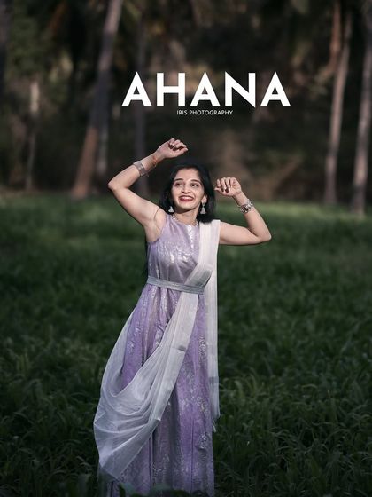 A portrait from the "Ahana" series, set in a lush green field. The dramatic lighting and the model's pose create a cinematic and slightly mysterious mood.