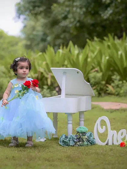 Holding two roses, this little girl stands by the miniature piano during her first birthday photoshoot. I focus on capturing these small, curious details that showcase your child's budding personality.