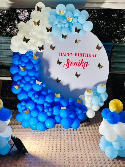 A simple yet elegant birthday decoration in shades of blue and white. This setup features a circular backdrop personalized with the name, accented with gold butterflies and two small balloon pillars.