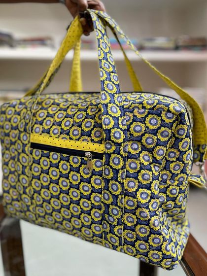 A detail shot of the travel bag's zippered pocket, featuring a contrasting yellow zipper on the dark floral fabric.