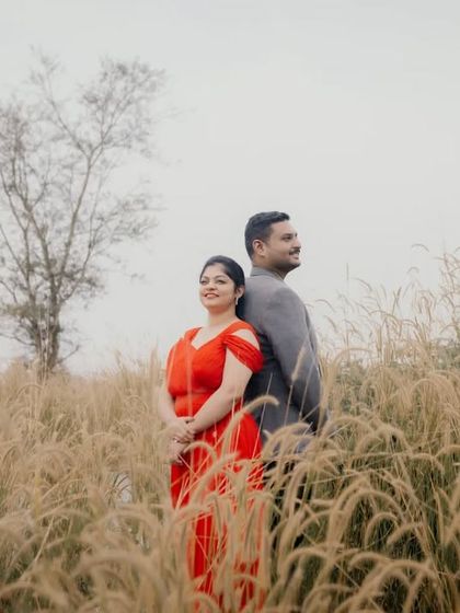 A couple stands back-to-back in a field of tall, golden grass, creating a stylish and composed portrait.