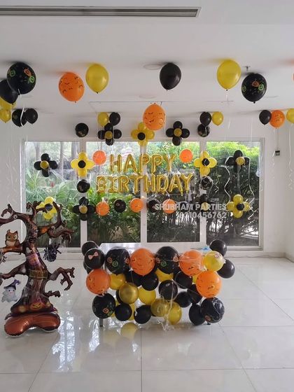 A spooky and fun Halloween themed birthday party with a haunted tree prop and orange and black balloons.