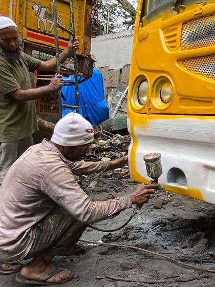Craftsmen painting the bus for the "Wonder on Wheels" project. This initiative involved local artisans and mechanics, turning a decommissioned bus into a vibrant yellow school on wheels.