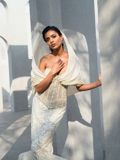 Another view of the ivory hooded gown, where delicate embroidery catches the light, tracing gentle patterns across its surface. It is a piece that exists in the space between movement and stillness.