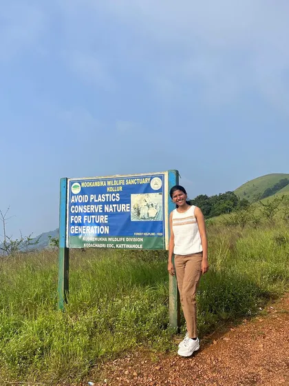 A trekker stands by a sign for the Mookambika Wildlife Sanctuary, reminding us to conserve nature.