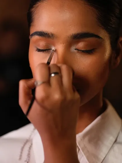 An artist applies a touch of highlighter to the inner corner of a model's eye, a key technique for making the eyes pop on the runway.