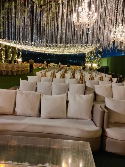 An elegant lounge seating arrangement under a sky of hanging crystals and chandeliers. The neutral-toned sofas and clear acrylic tables create a sophisticated space for guests to mingle.