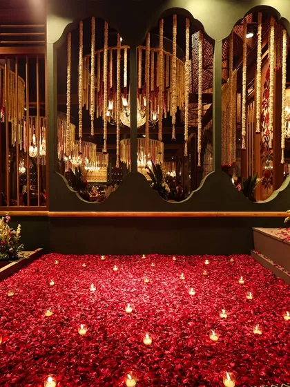 A path of romance. A carpet of red rose petals dotted with candles leads the way, reflecting in the mirrored walls adorned with hanging floral strings, creating an infinitely magical effect.