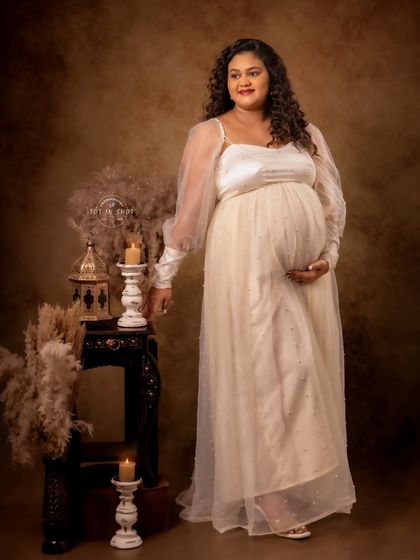A standing portrait showcasing the elegant silhouette of the mother-to-be in a sheer-sleeved cream gown.