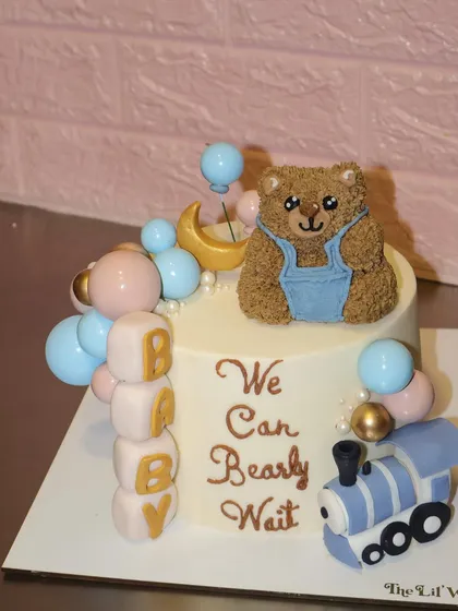 We can bearly wait. This adorable baby shower cake features a sculpted teddy bear, pastel pink and blue balloons, and a tiny toy train, making it perfect for welcoming a new baby.