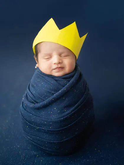 A little king in the making. This newborn is wrapped snugly in a starry blue swaddle, dreaming royally. The simple paper crown adds a playful and adorable touch.