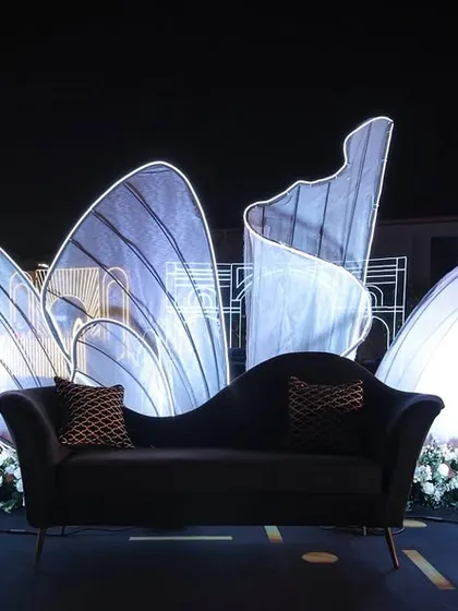A chic and modern stage seating area for the couple, with an illuminated, abstract shell-like backdrop that glows against the night sky.