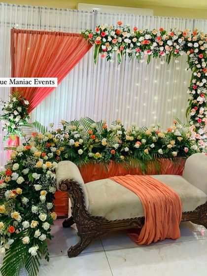 A lavish engagement stage decoration featuring a full frame of peach and white flowers. The ornate divan seating adds a touch of royalty to the beautiful setup.