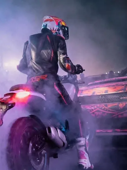 The view from behind the handlebars during a night show. The combination of a powerful motorcycle, a custom car, and atmospheric smoke creates a thrilling, immersive experience for the audience.