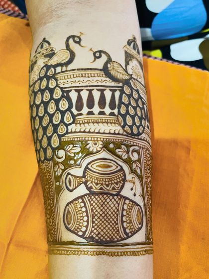 A detailed look at an armband design featuring dancing peacocks on a balcony and a dhol drum motif below.