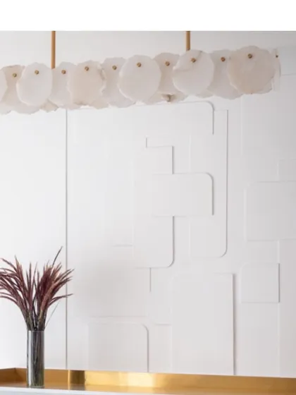 The beauty of minimalism. A stunning shell-like chandelier hangs against a white, geometrically paneled wall, creating a focal point that is both intricate and understated.