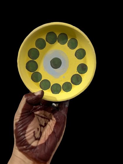 Holding up a freshly painted plate with a simple, cheerful dot pattern. My hands are often covered in paint or clay, a testament to the hands-on nature of my craft.
