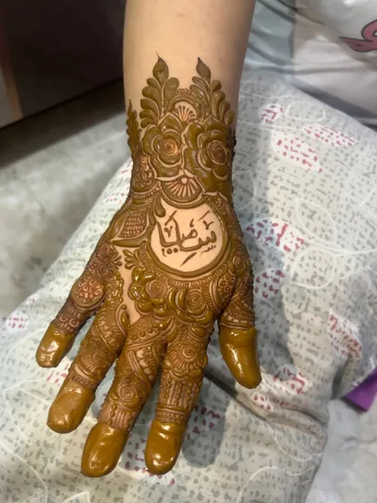 I can beautifully write names and initials in your mehendi. Here, a name in elegant Arabic script is the centerpiece of a detailed floral design on the hand.
