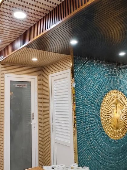 This corner of our showroom features a stunning 3D wall art piece in teal and gold, complemented by wooden louvers on the walls and ceiling.