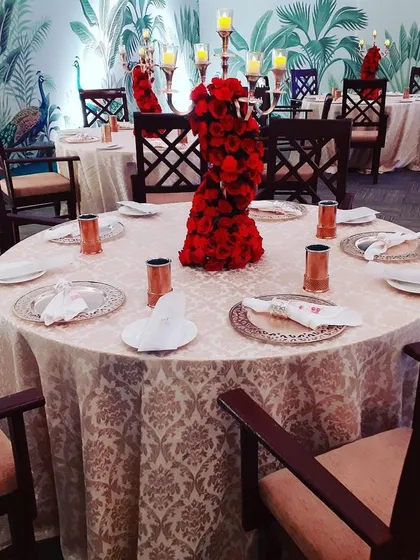Attention to detail is key for an elegant guest experience. This table setting features a striking red rose centerpiece, candelabras, and patterned linens, all set against a custom tropical-themed wallpaper for a cohesive look.