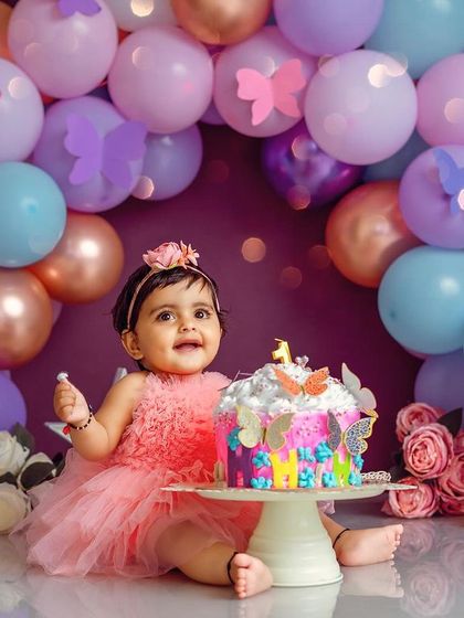 This little butterfly is ready for her cake. The colorful butterfly cake and balloon arch create a whimsical and beautiful setting for her first birthday.