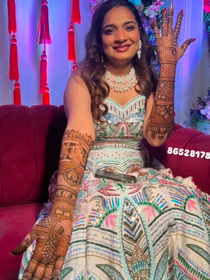 A happy bride showing her full-arm bridal mehndi, which includes story elements and traditional patterns.