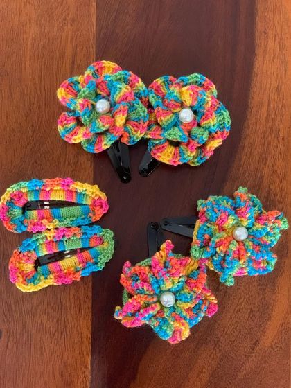 A set of my rainbow-themed floral hair clips. The vibrant, multi-colored yarn and central pearl detail make these clips a fun and festive accessory.