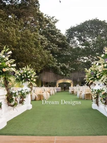 The grand entrance to the main lawn, framed by white pillars topped with large, dramatic floral arrangements. This creates a formal and impressive entryway for the wedding celebration.