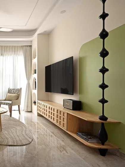 The TV unit in this living room features a unique color-blocked background in soft green, with a sculptural black element dividing the space. The wooden console adds warmth and texture.