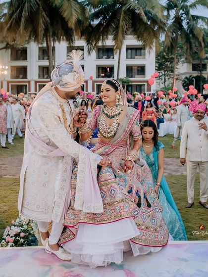 The groom helps his bride onto the stage for the Varmala ceremony, a gesture of care and partnership at their beautiful outdoor wedding.