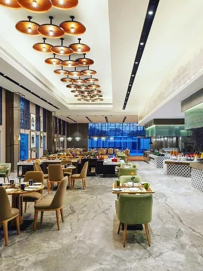 In this all-day dining restaurant at the DoubleTree by Hilton, the lighting design creates a dynamic and inviting atmosphere. A custom cluster of copper-toned pendants provides warm, intimate light over the main seating area, while integrated architectural lighting highlights the room's scale and details.