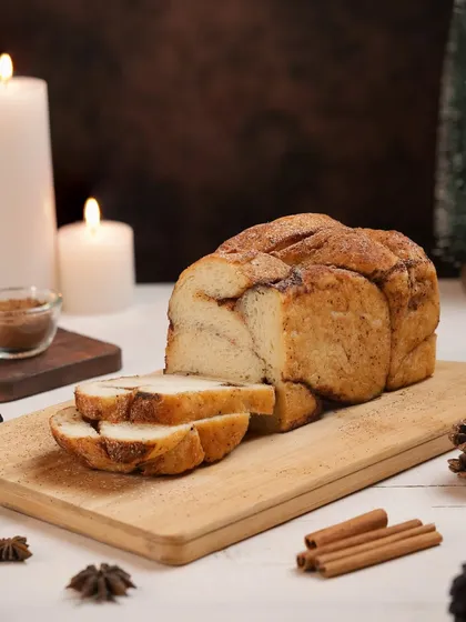 A loaf of cinnamon bread styled for a Christmas-themed shoot with candles and pine cones. We create a cozy, wintery atmosphere perfect for seasonal bakery items.