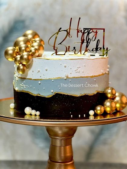 An elegant tall cake with a black, grey, and white theme, decorated with gold and pearl bubbles. This was a chocolate truffle cake for a sophisticated birthday celebration.